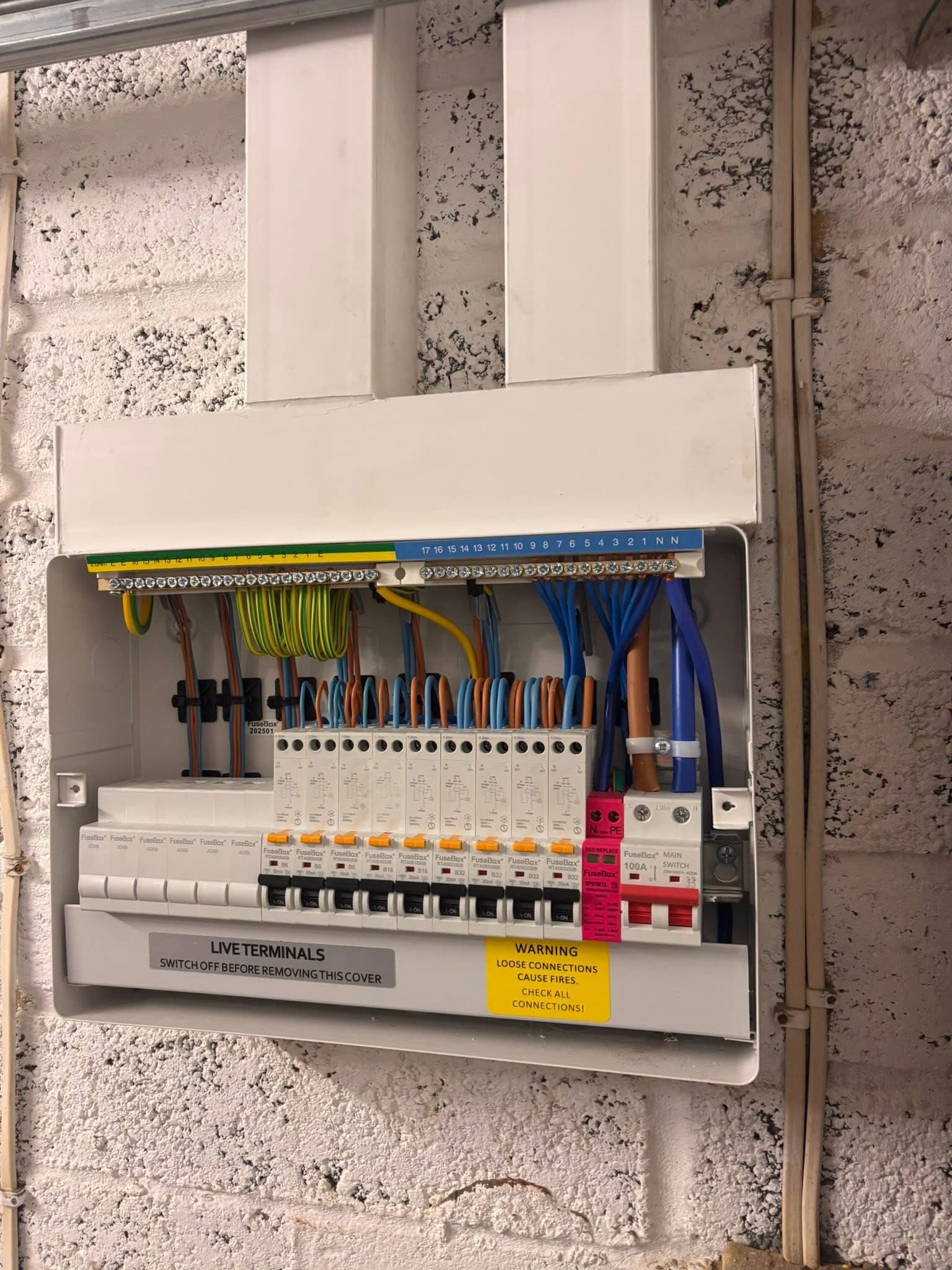 Open electrical fuse box showing circuit breakers and colorful wiring on a white wall.
