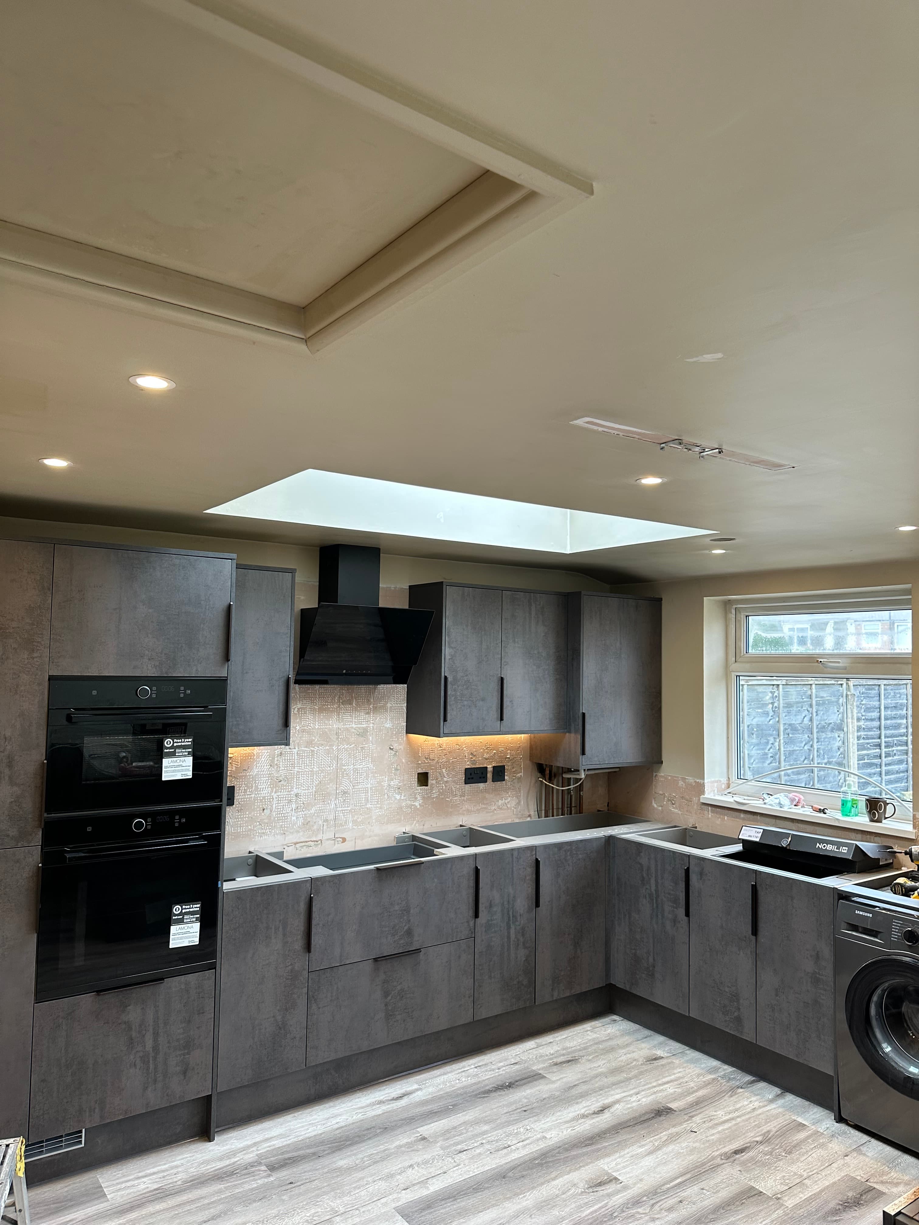Modern kitchen featuring dark grey cabinets, black appliances, light wood floors, and a bright skylight.