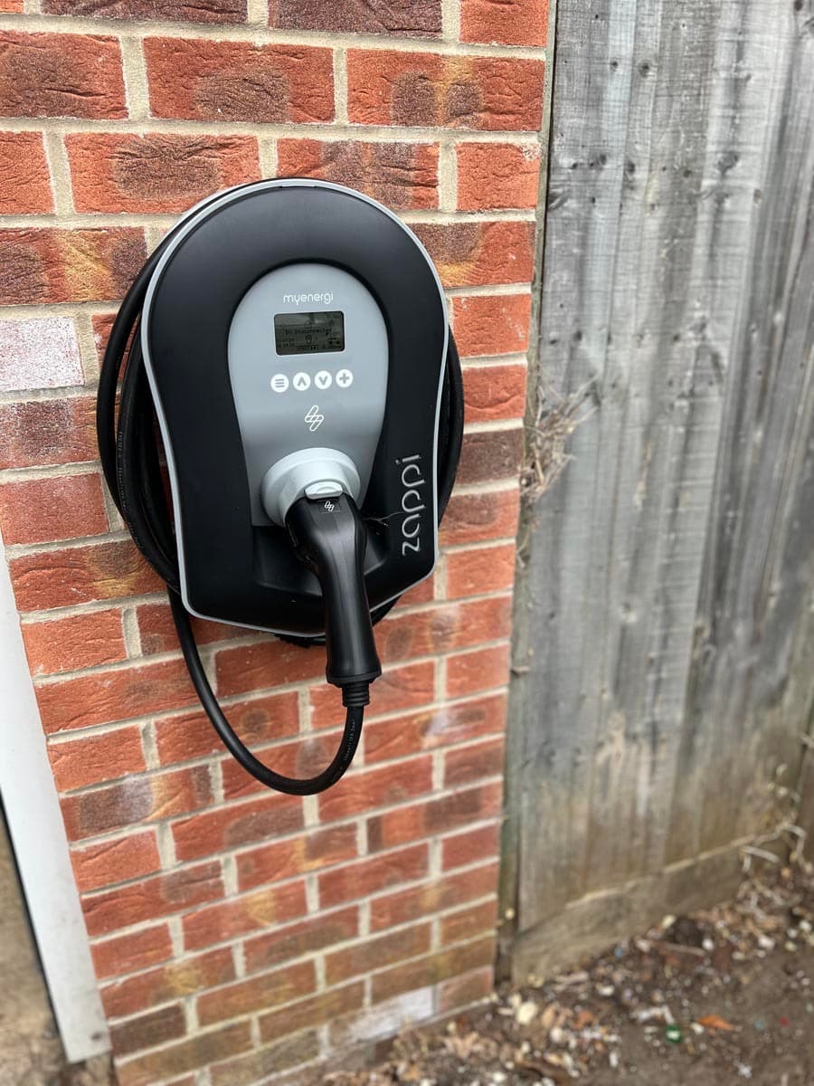Zappi electric vehicle charger by myenergi mounted on a red brick wall with cable.
